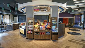 A modern kiosk with a variety of snacks and beverages, a sign for a 24/7 market, and a breakfast area with a view of the cityscape.