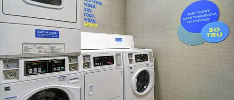 A laundry facility with multiple washing machines and dryers, a wall with laundry instructions, and a motivational quote.