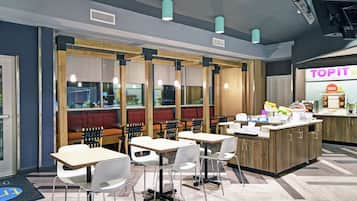 Um restaurante moderno com mesas e cadeiras de madeira, um balcão com alimentos e um quadro de menu visível.