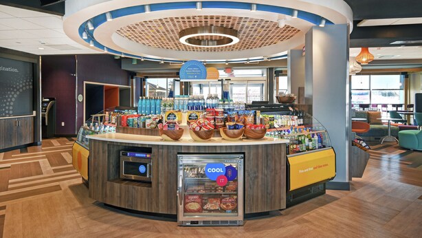 A modern food court with a central counter, refrigerated display, and seating area.