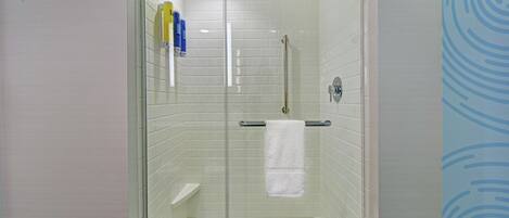 Un box de ducha con paredes de azulejos blancos, una puerta de vidrio y una toalla blanca colgada en un toallero plateado.