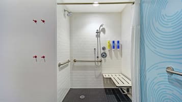 A small, accessible shower area with white tiled walls, a handheld showerhead, and a grab bar.