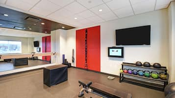 Un gimnasio con equipamiento de ejercicio, una televisión y una pantalla instalada en la pared.