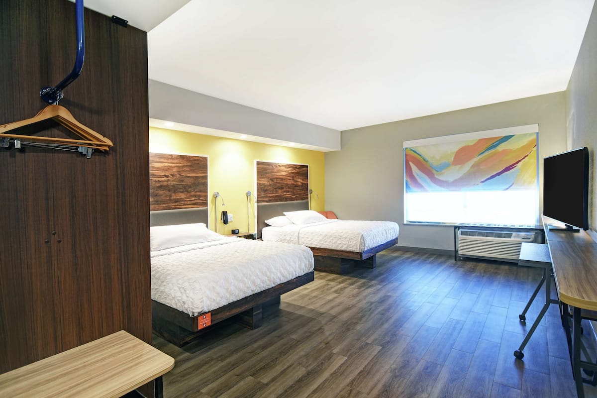Une chambre d’hôtel avec deux lits, une commode en bois, un bureau, une télévision et un grand tableau abstrait accroché au mur.