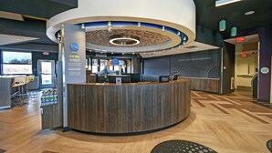 A modern hotel reception area with a curved desk, a digital display, and a view of the outside.