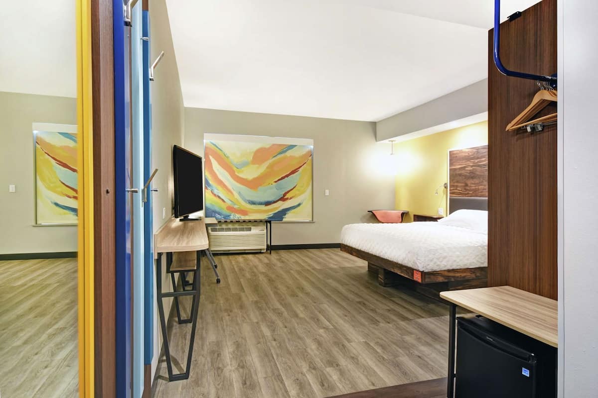 Une chambre d’hôtel équipée d’un lit, d’un bureau, d’une chaise, d’une télévision et décorée avec des œuvres d’art abstraites.