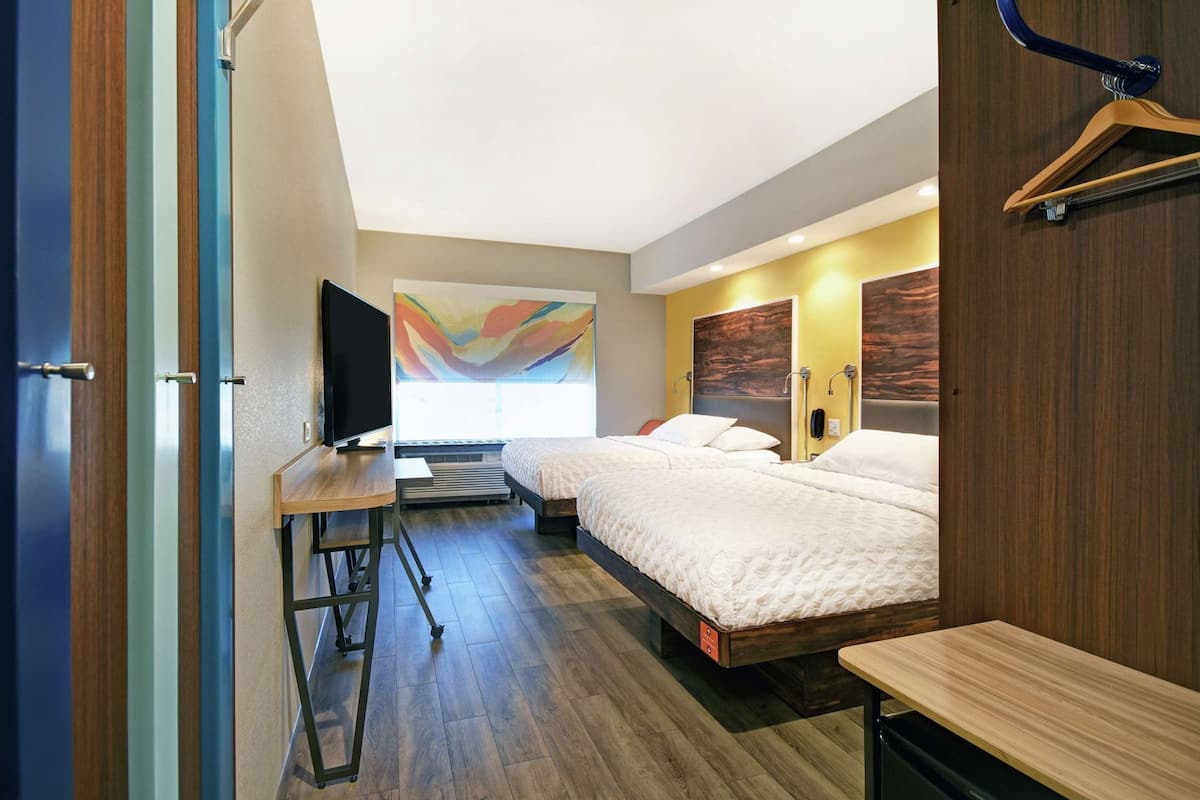 Une chambre d’hôtel avec deux lits, un bureau, une télévision et un grand tableau abstrait accroché au mur.