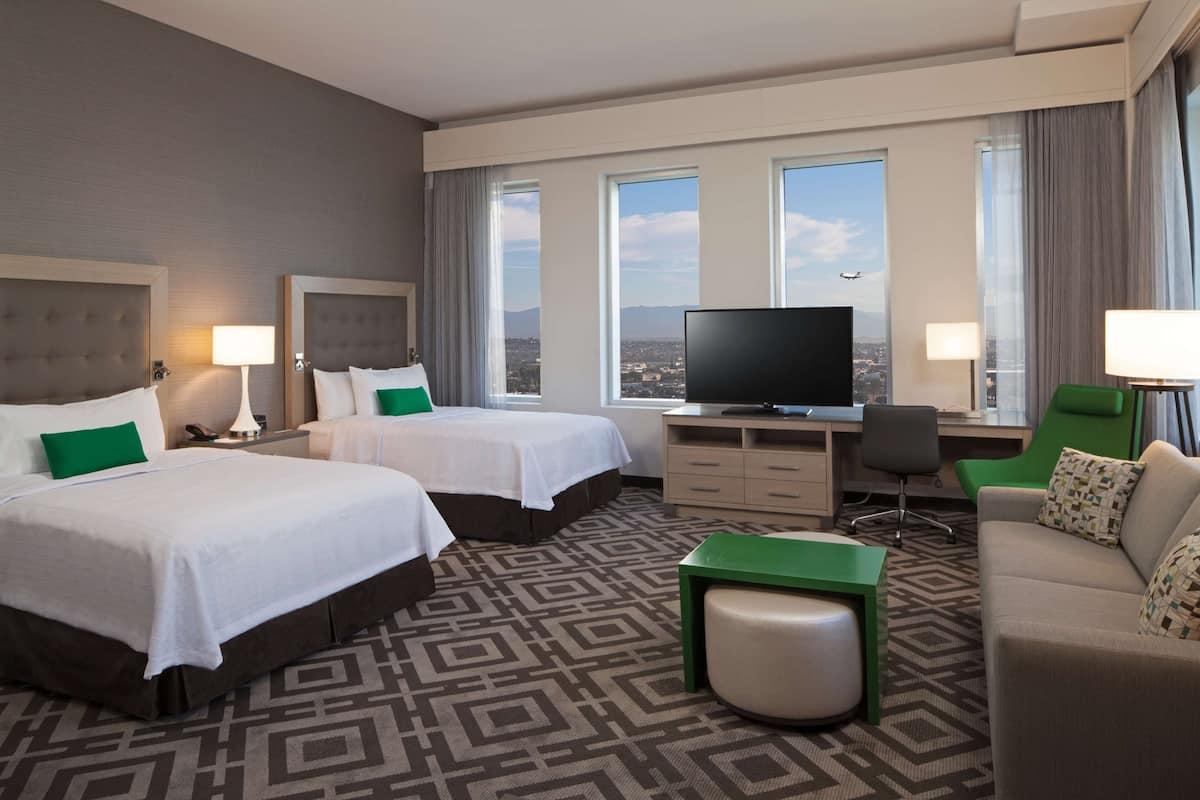 Ein Hotelzimmer mit zwei Betten, einem Schreibtisch, einem Fernseher und Blick auf die Stadt.