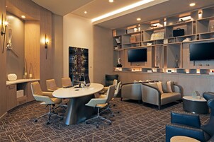 A modern conference room with a round table, comfortable seating, and a TV on the wall.