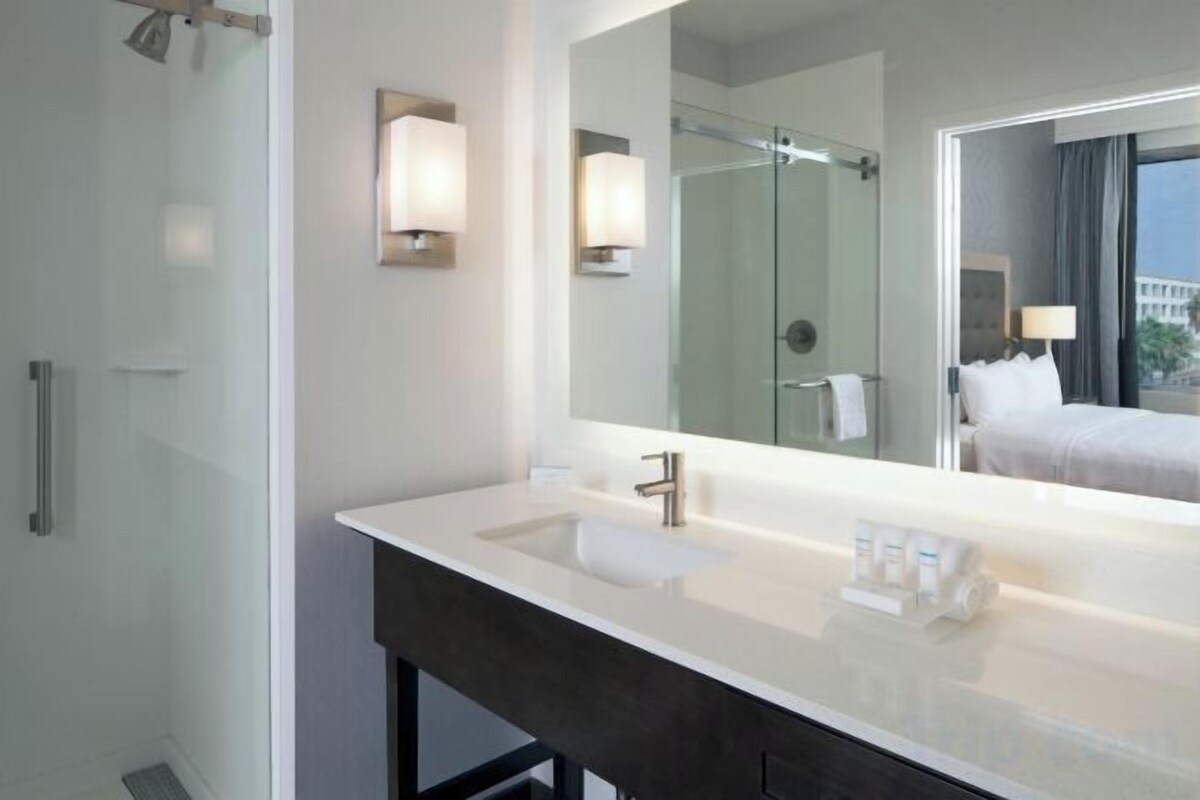 A hotel bathroom with a large mirror, a sink, and a shower.