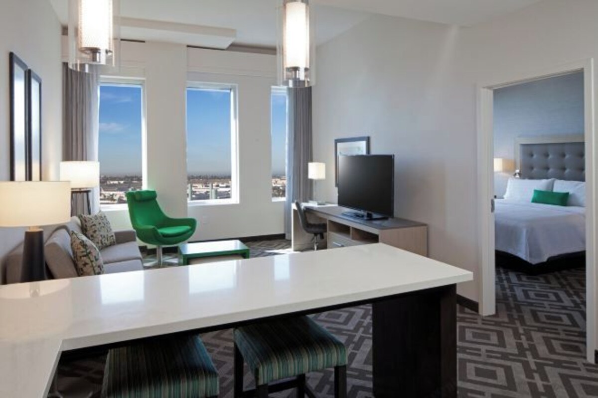 A hotel room with a large bed, a desk with a computer, a green chair, and a TV.