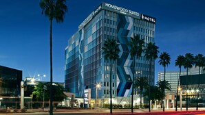 Un hotel moderno con una fachada geométrica distintiva, situado en un entorno urbano con palmeras y farolas.