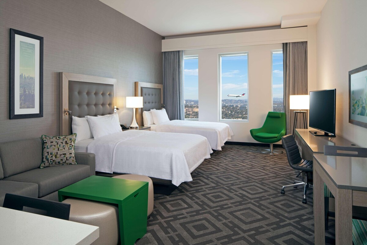 A hotel room with two beds, a sofa, a desk, a chair, and a TV.