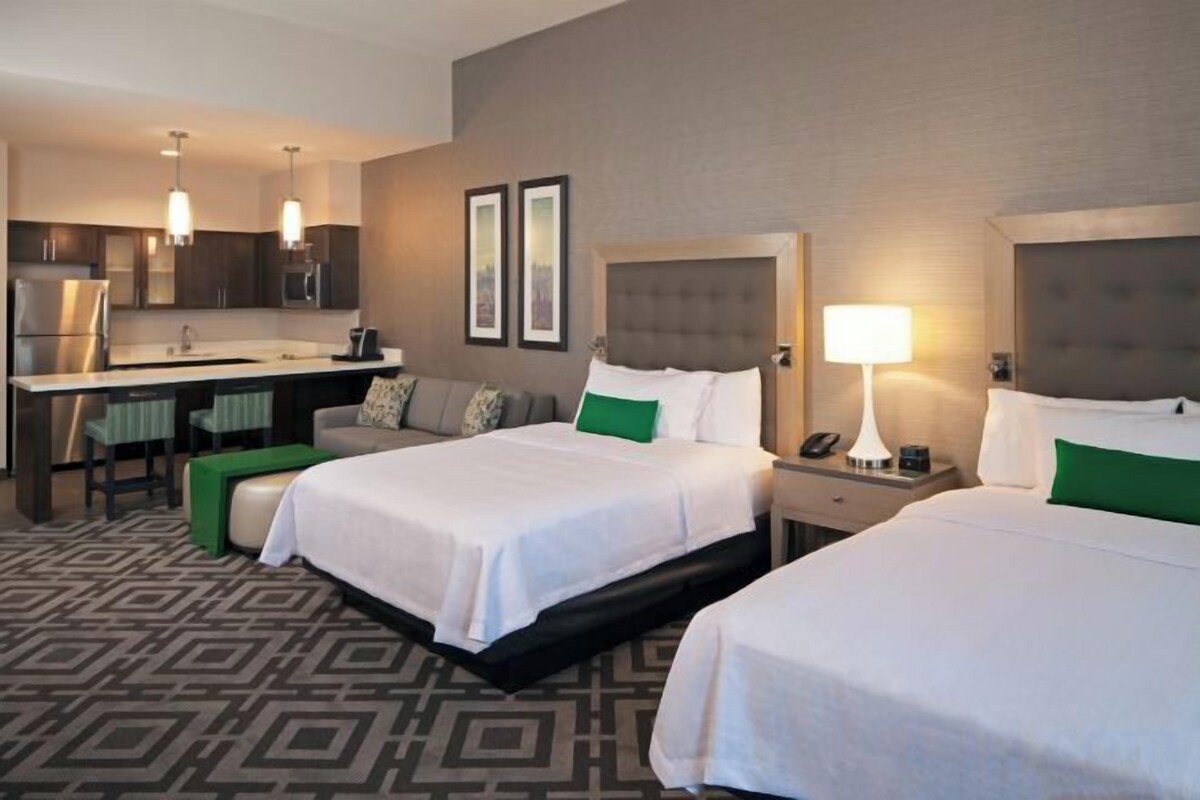 A hotel room with two beds, a kitchenette, and a sitting area with a sofa and chairs.