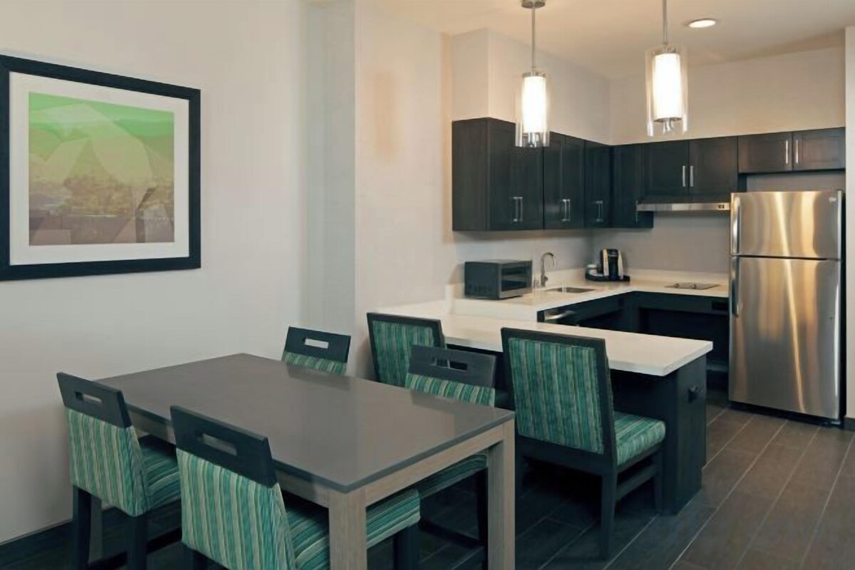 A modern kitchen with dark cabinets, a stainless steel refrigerator, and a dining area with a table and chairs.