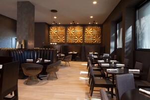 A modern restaurant interior with dark-toned booths, contemporary chairs, and a patterned wall feature.