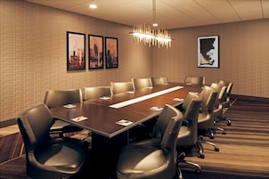 Una sala conferenze con un lungo tavolo, diverse sedie, quadri appesi alle pareti e un lampadario moderno.