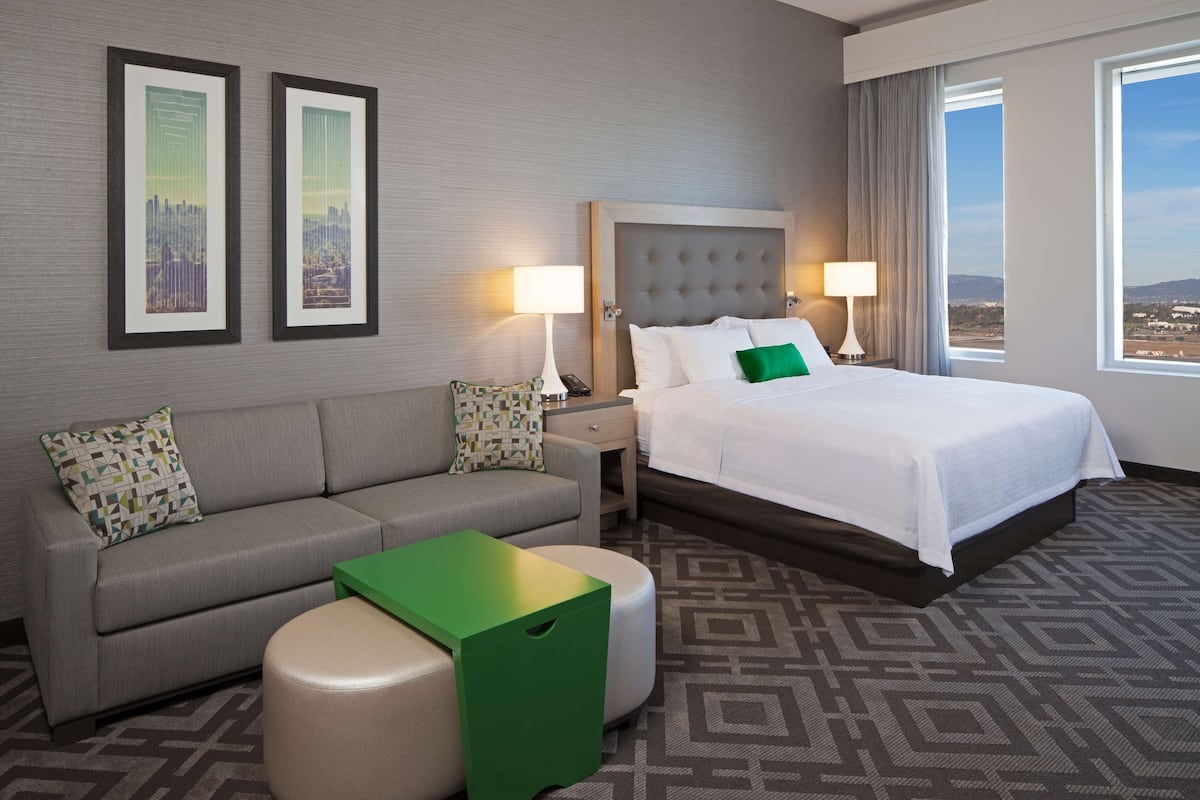Ein Hotelzimmer mit Bett, Sofa, zwei Nachttischen und Blick auf die Stadt.