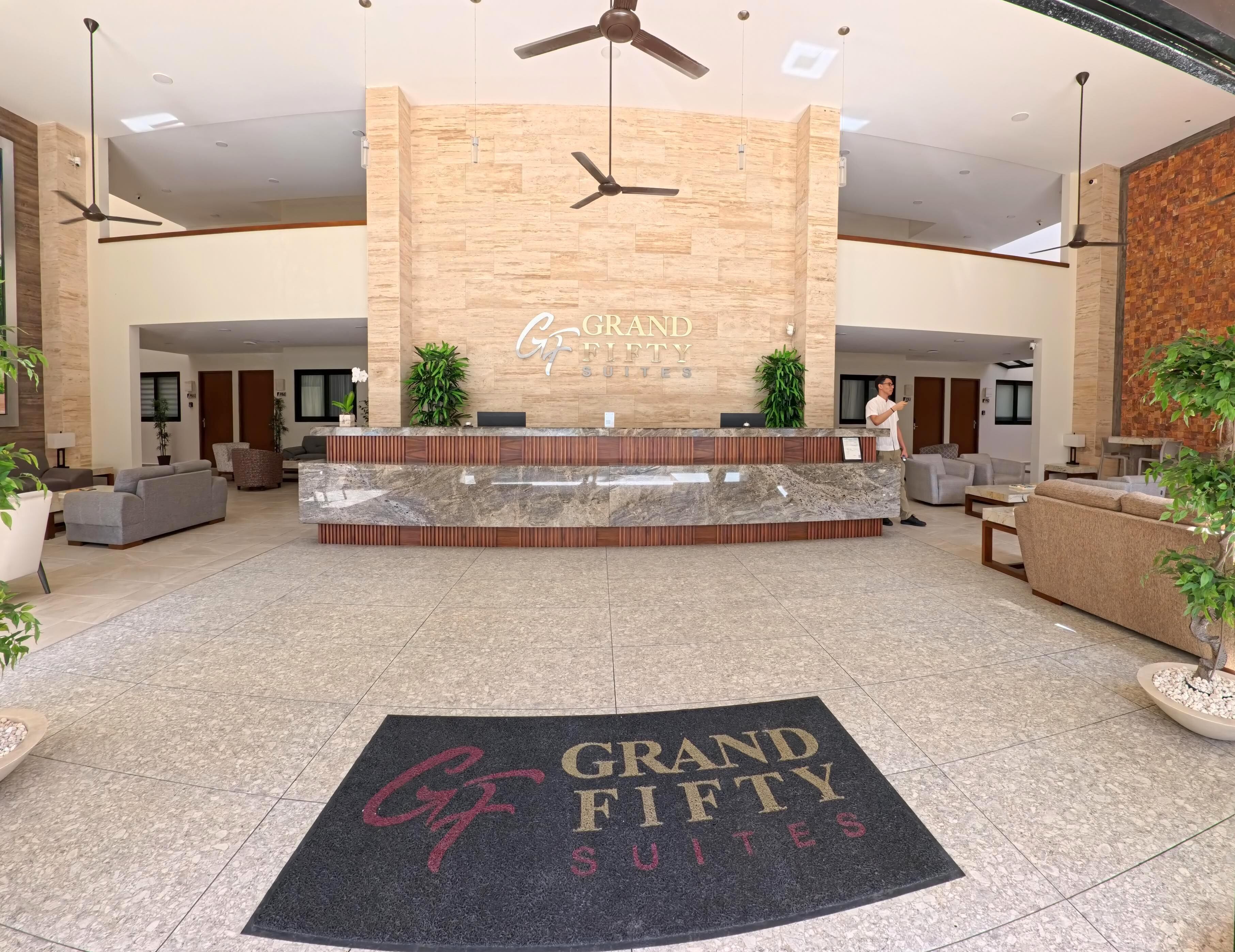 Ein Hotel-Empfangsbereich mit einer Rezeption, einer Sitzecke und einem großen Schild mit der Aufschrift 'Grand Fifty Suites'.