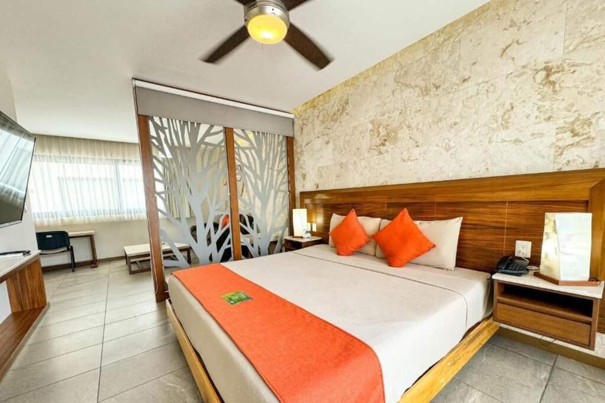Een hotelkamer met een bed, een bureau, een stoel, een televisie en een plafondventilator.
