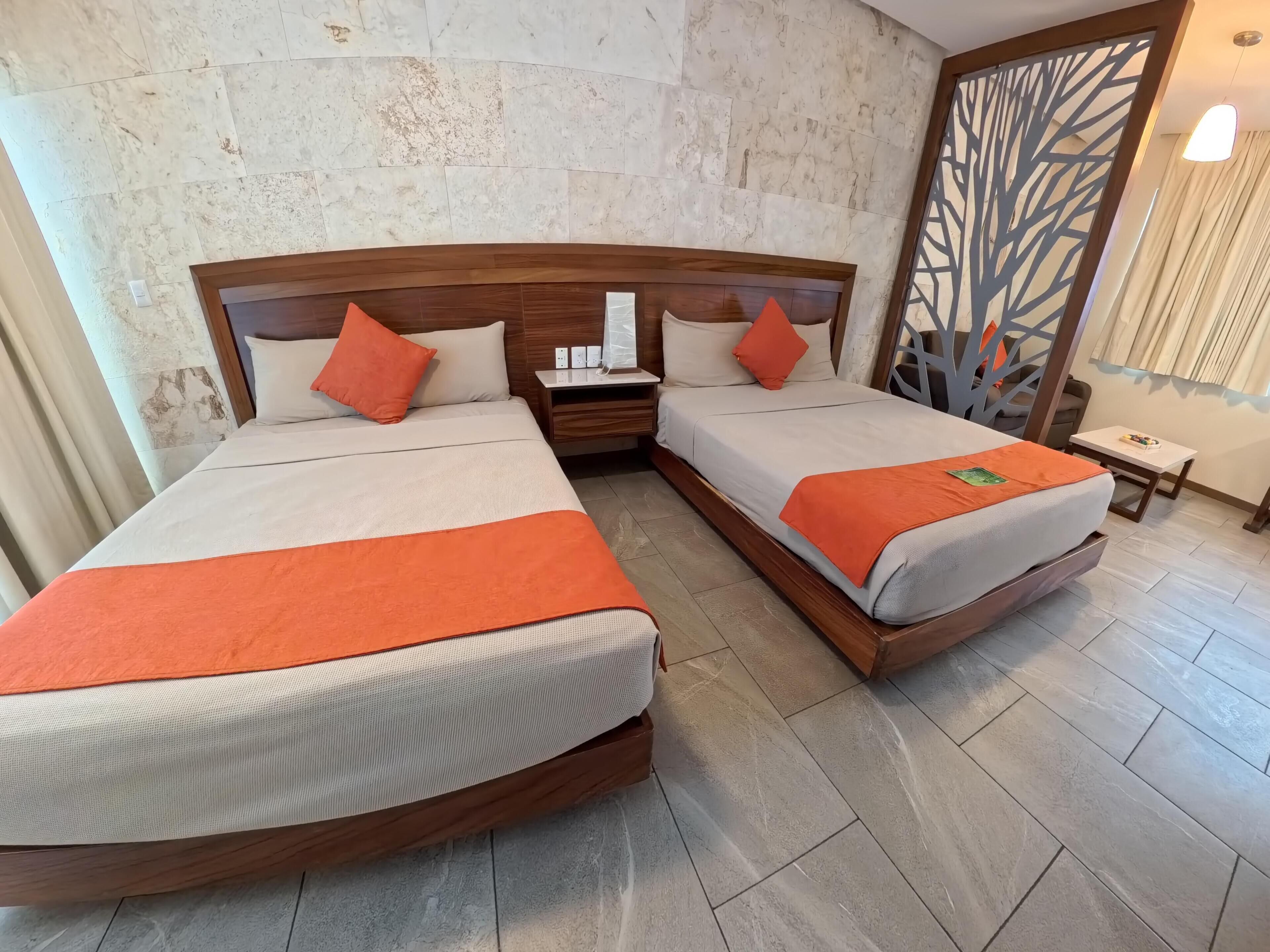 Habitació d'hotel amb dos llits, una tauleta de nit, una taula petita i un panell decoratiu a la paret.