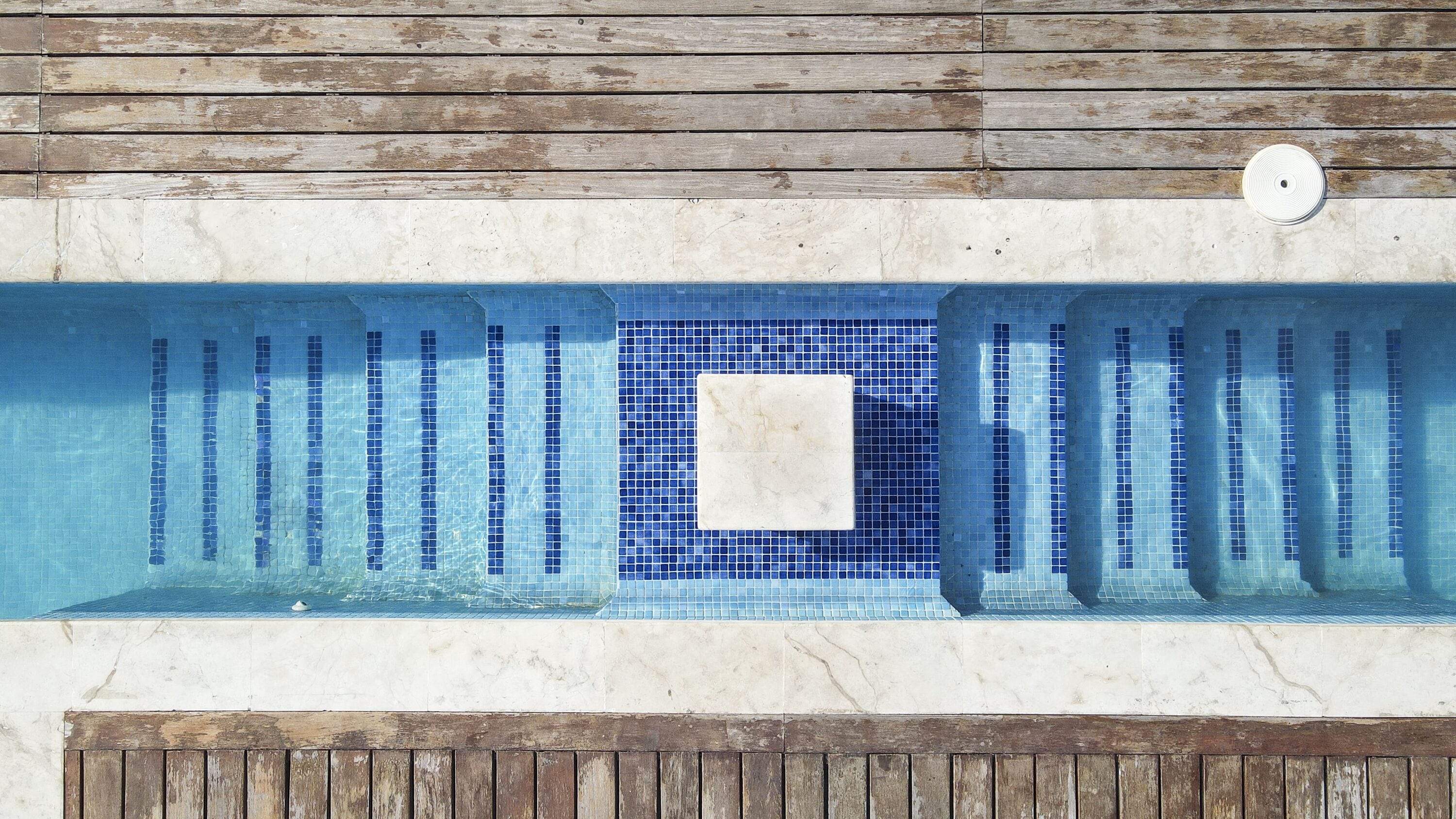 A swimming pool with a tiled deck and a wooden deck surrounding it.