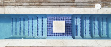 A swimming pool with a tiled deck and a wooden deck surrounding it.