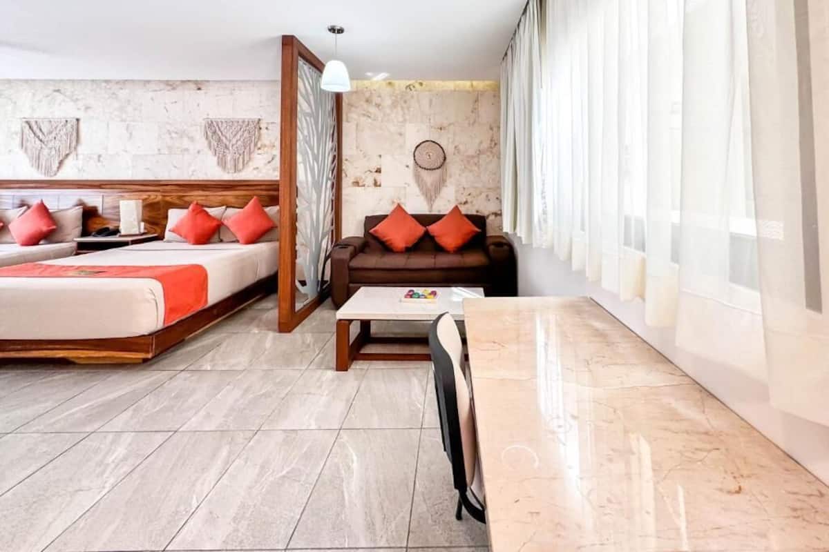 Een hotelkamer met een bed, een sofa, een eettafel en een groot raam met gordijnen.