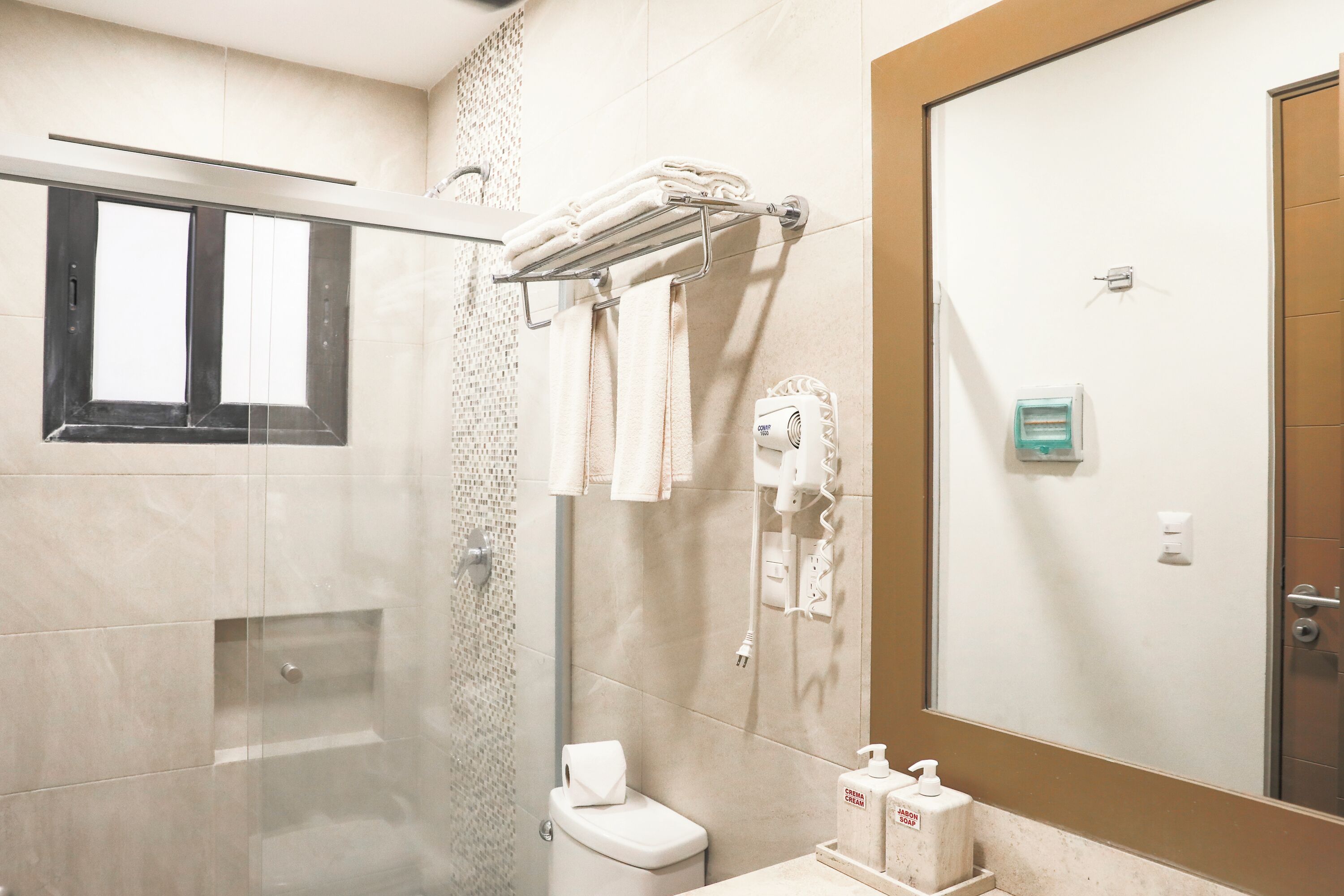 Une salle de bain moderne avec une douche à parois de verre, des toilettes, un porte-serviettes avec des serviettes pliées, un sèche-mains et un distributeur de savon.