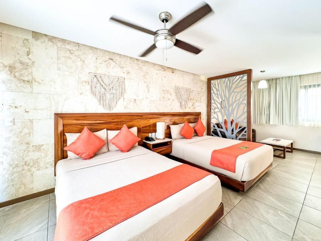 A hotel room with two beds, a ceiling fan, a large mirror, and a view of the outside.