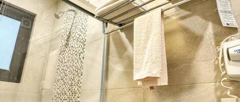 A bathroom with a glass shower enclosure, a towel rack with folded towels, and a wall-mounted phone.