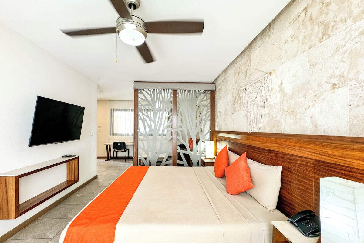 Een hotelkamer met een bed, een televisie, een bureau, een stoel en een plafondventilator.