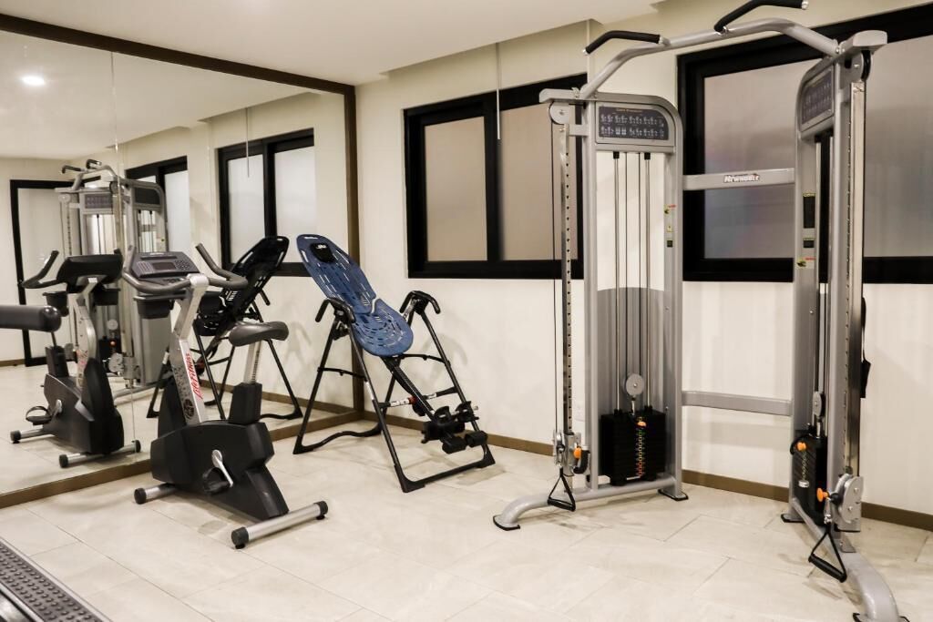 Een fitnessruimte met diverse trainingsapparaten, een loopband en een spiegelwand.