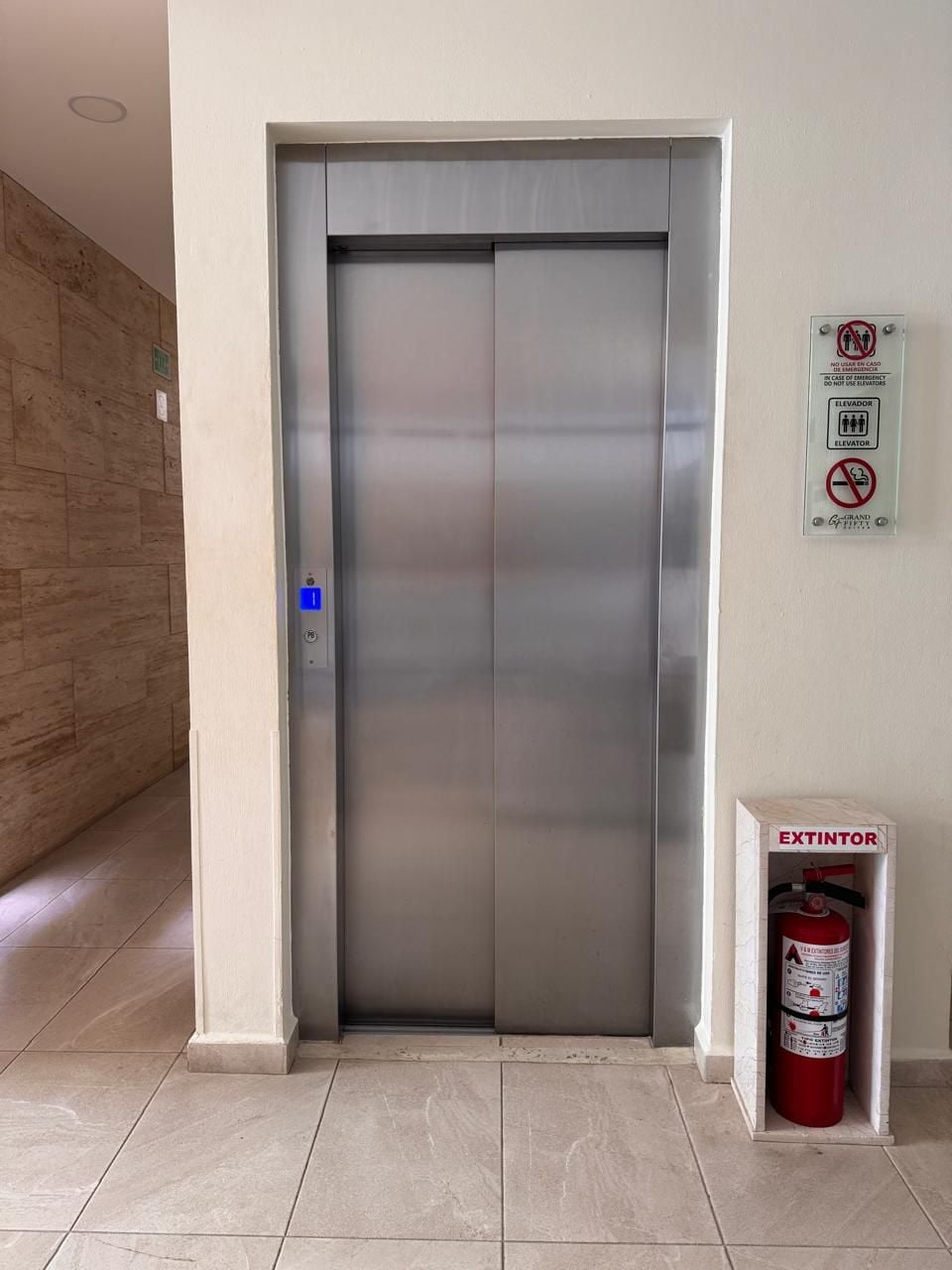 An elevator with a fire extinguisher mounted on the wall beside it.
