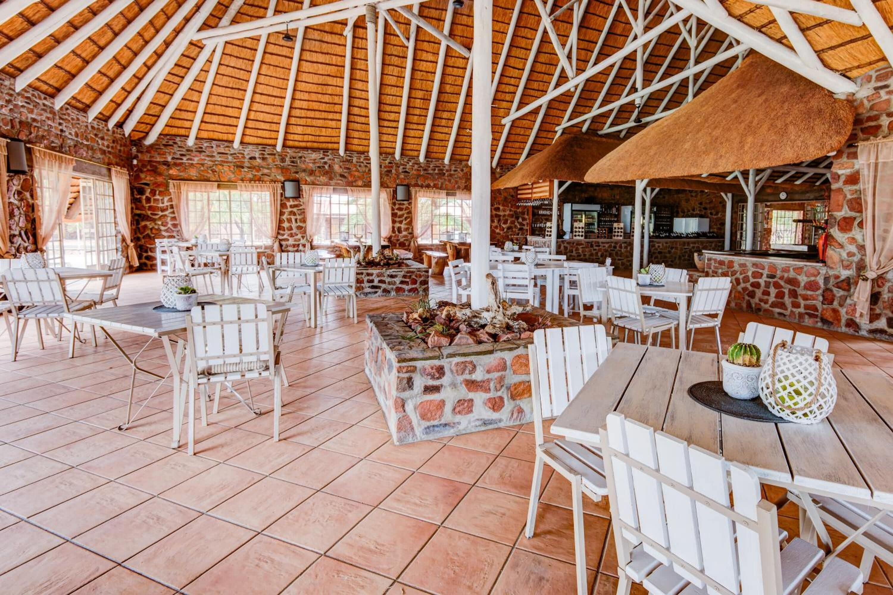 A spacious outdoor dining area with stone walls, wooden tables, and white chairs.