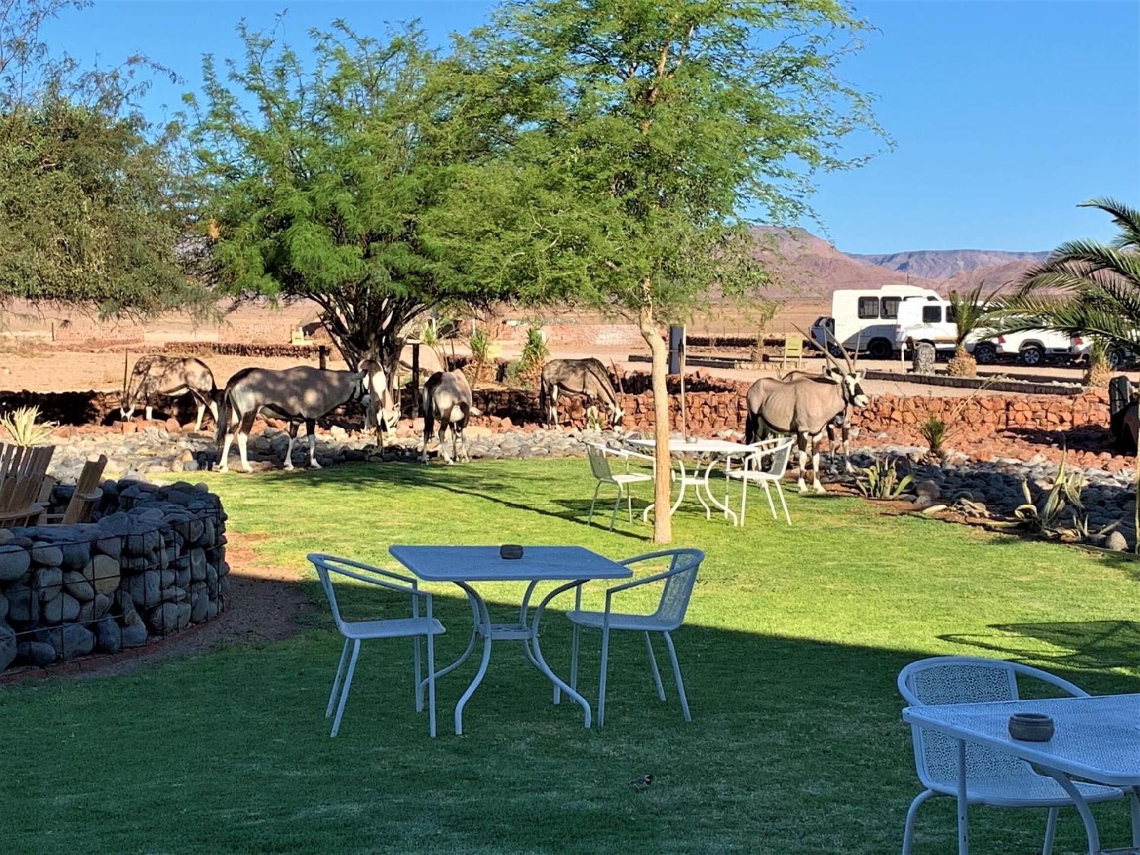Une terrasse avec une table et des chaises, entourée d’un mur de pierre et d’une pelouse.