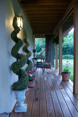 A wooden deck with a spiral topiary, potted plants, and a bench. - Two Hearts Inn (Edmond)
