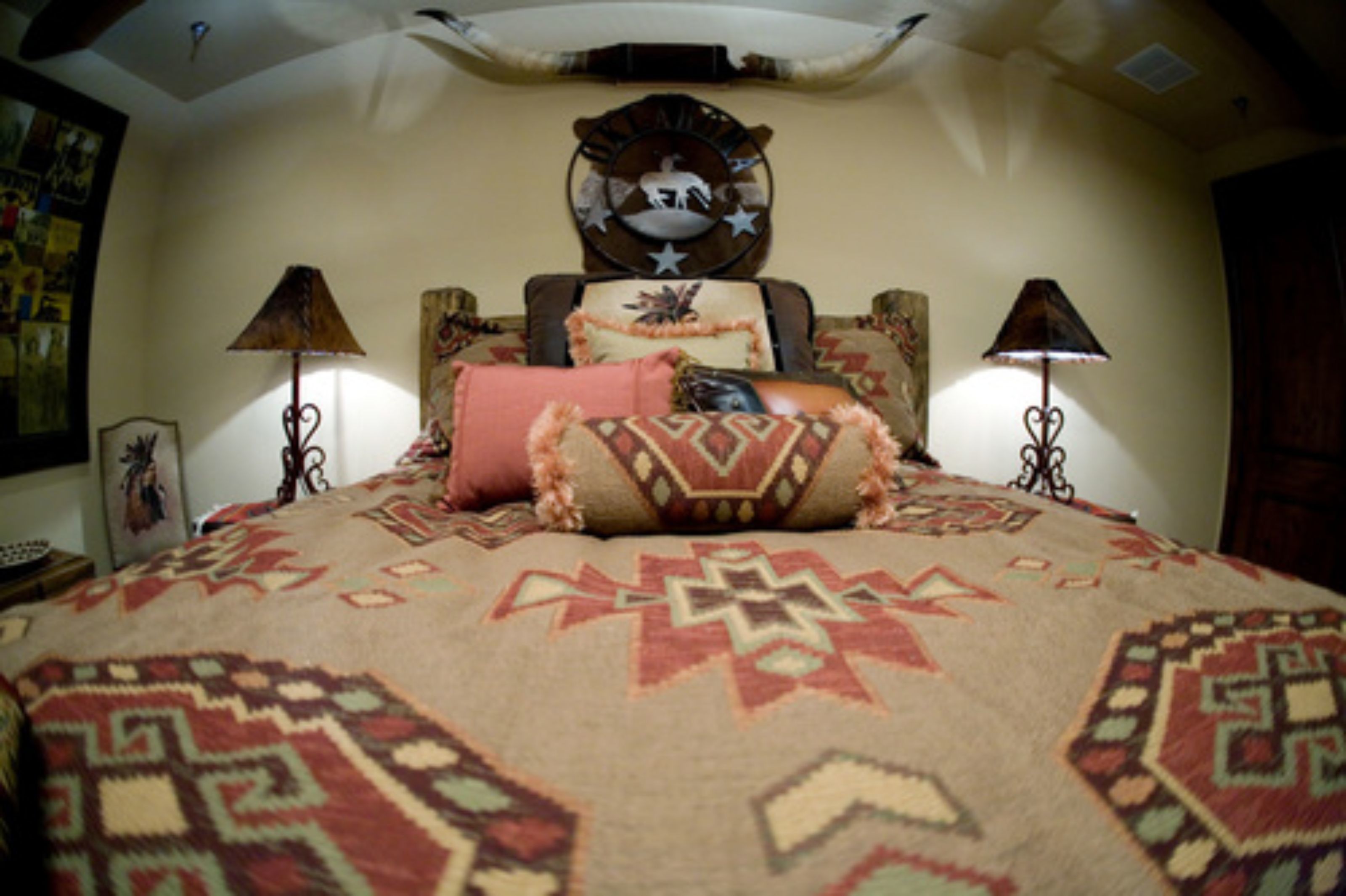 A bedroom with a large bed, patterned bedding, two wall-mounted lamps, and a decorative wall piece above the bed.