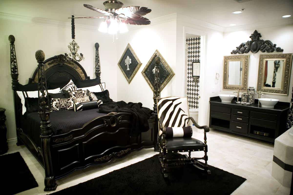 A bedroom with a large bed, a chair, a vanity with a mirror, and a ceiling fan.