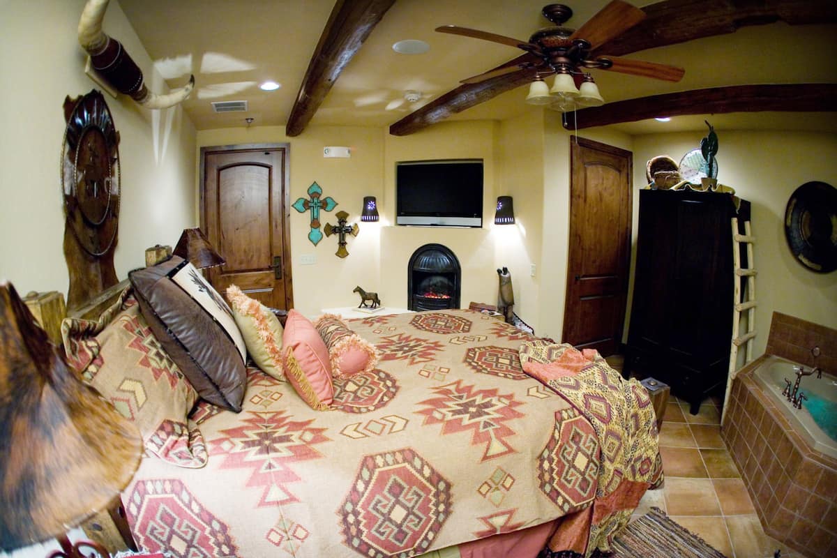 A bedroom with a bed, a fireplace, a wooden ceiling, and a TV mounted on the wall.