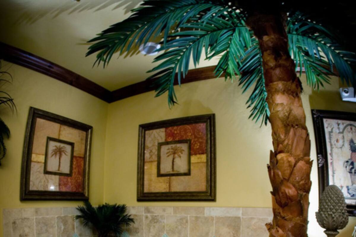 A bathroom with a large bathtub, a palm tree, and framed pictures on the wall.