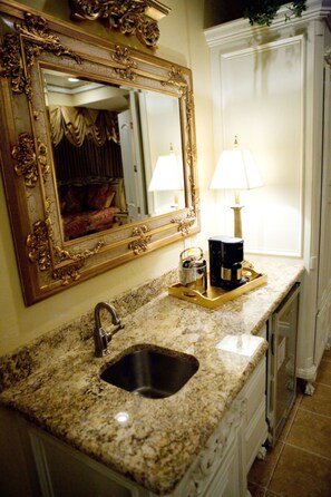 A bathroom with a granite countertop, a gold-framed mirror, a sink, and a white cabinet. - Two Hearts Inn (Edmond)