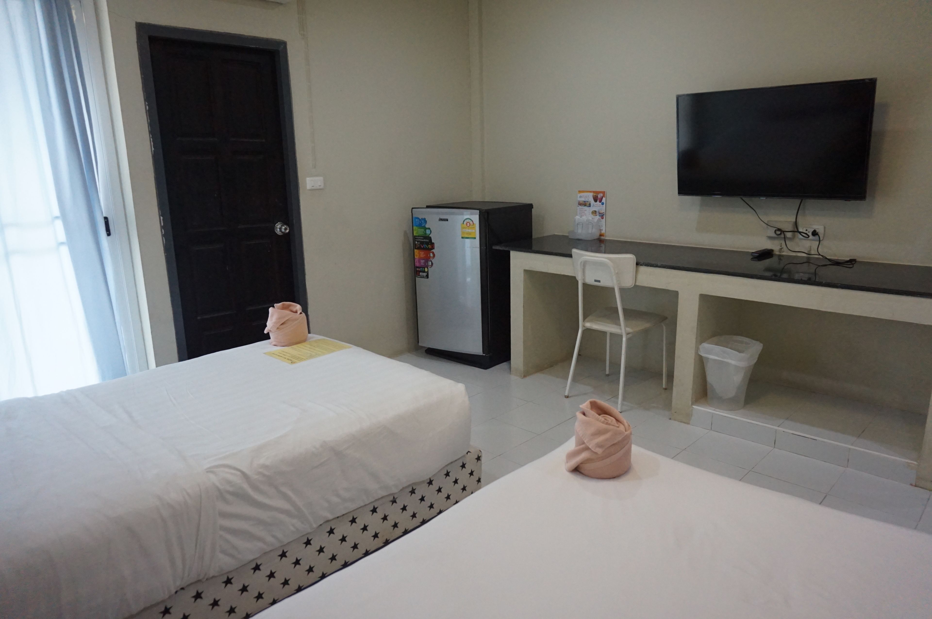 A hotel room with a bed, a desk with a chair, a TV, and a refrigerator.
