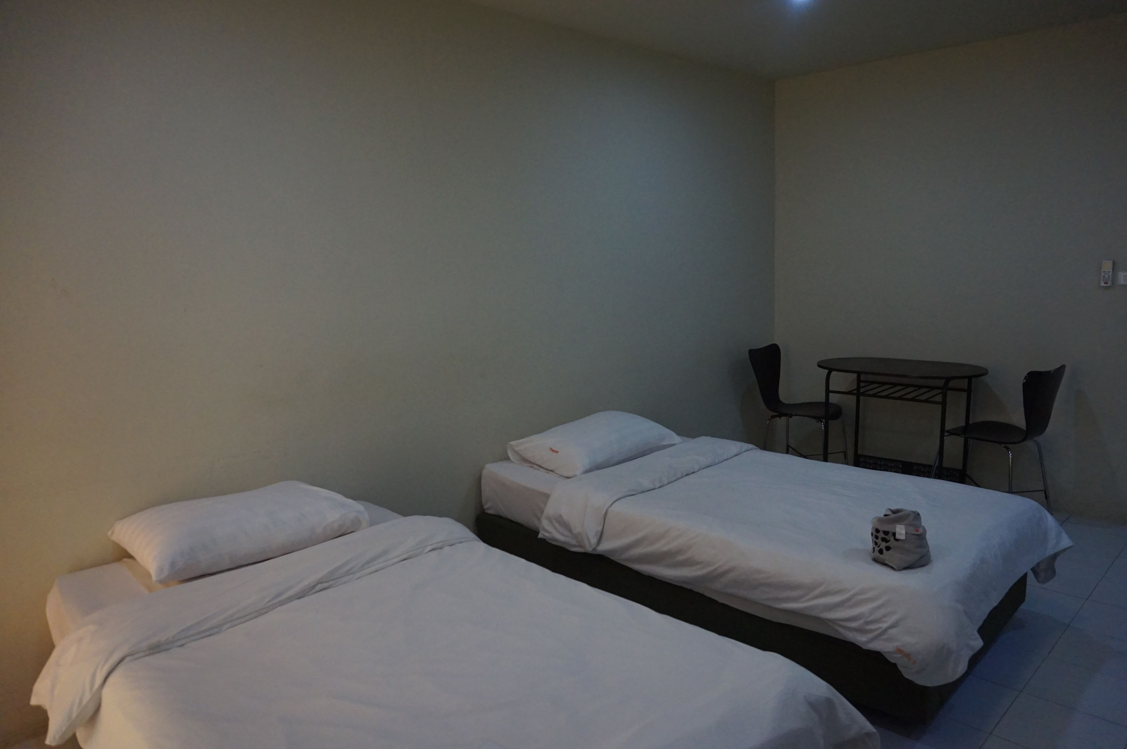 A room with two single beds, a small table with two chairs, and a white bag on one of the beds.