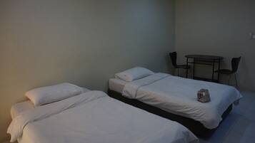 A room with two single beds, a small table with two chairs, and a white bag on one of the beds.