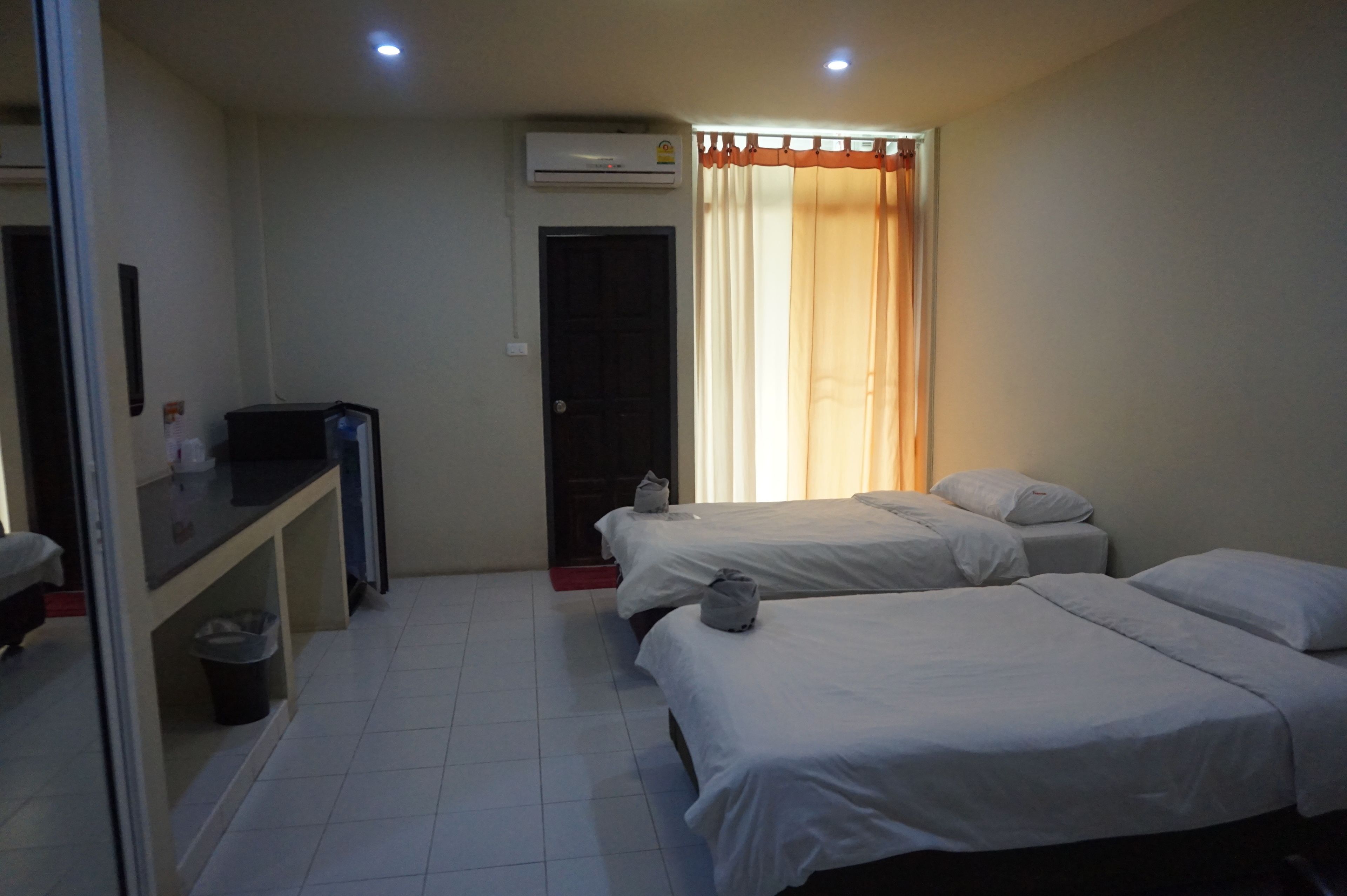 A hotel room with two beds, a desk, and an air conditioning unit.