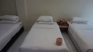 Habitación de hotel con dos camas individuales, cada una con ropa blanca y almohadas, una cama con una toalla doblada en el centro, y una mesita con un jarrón de flores.