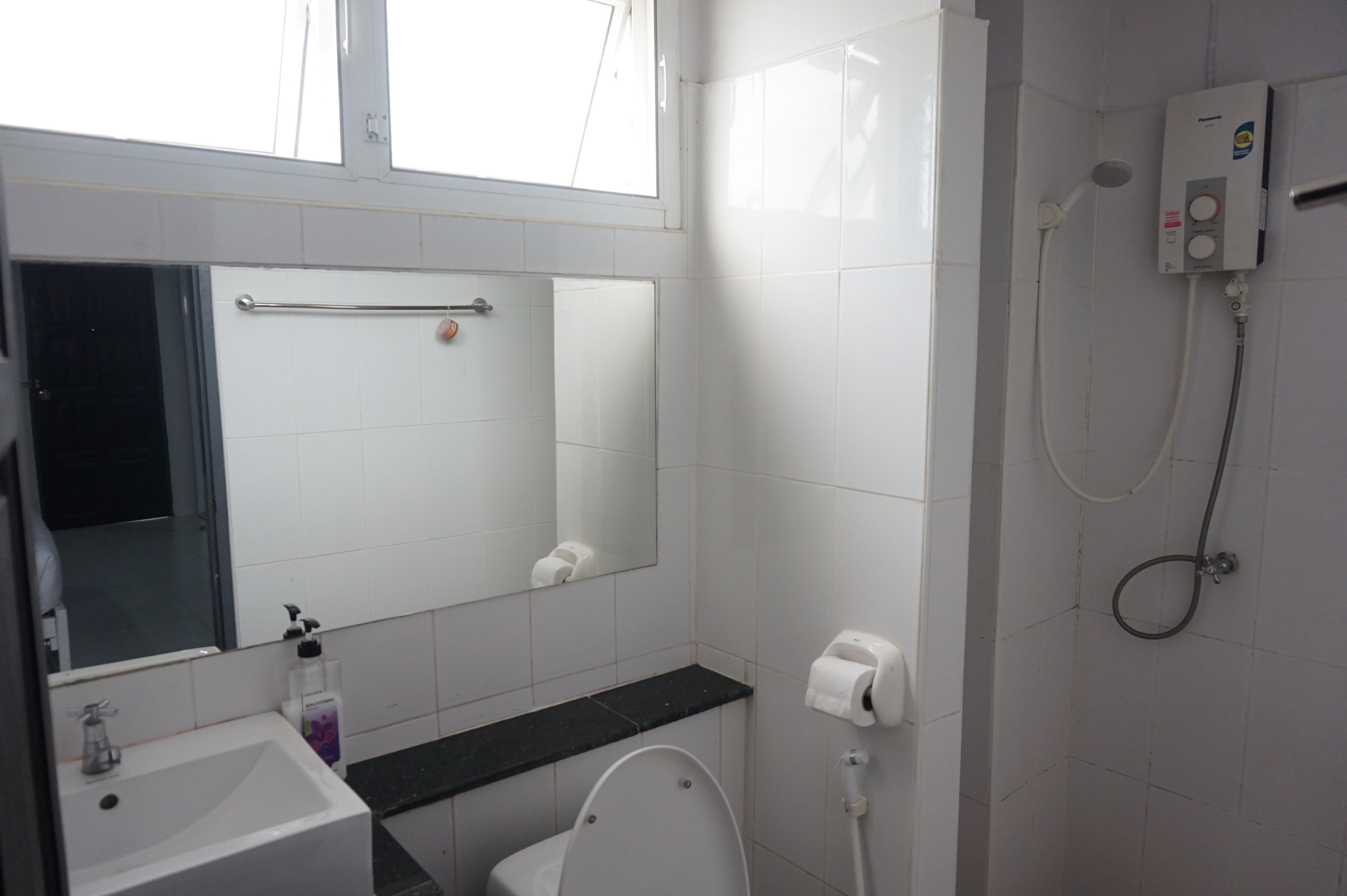 A bathroom with a sink, toilet, mirror, towel rack, and a shower unit.