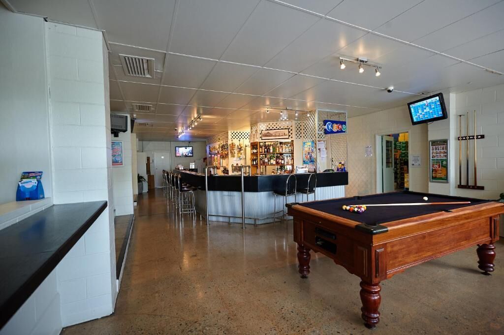 Una mesa de billar en una habitación con una zona de bar al fondo.