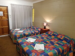 A hotel room with two beds, a wooden door, a curtain, a nightstand with a lamp, and a brick wall.